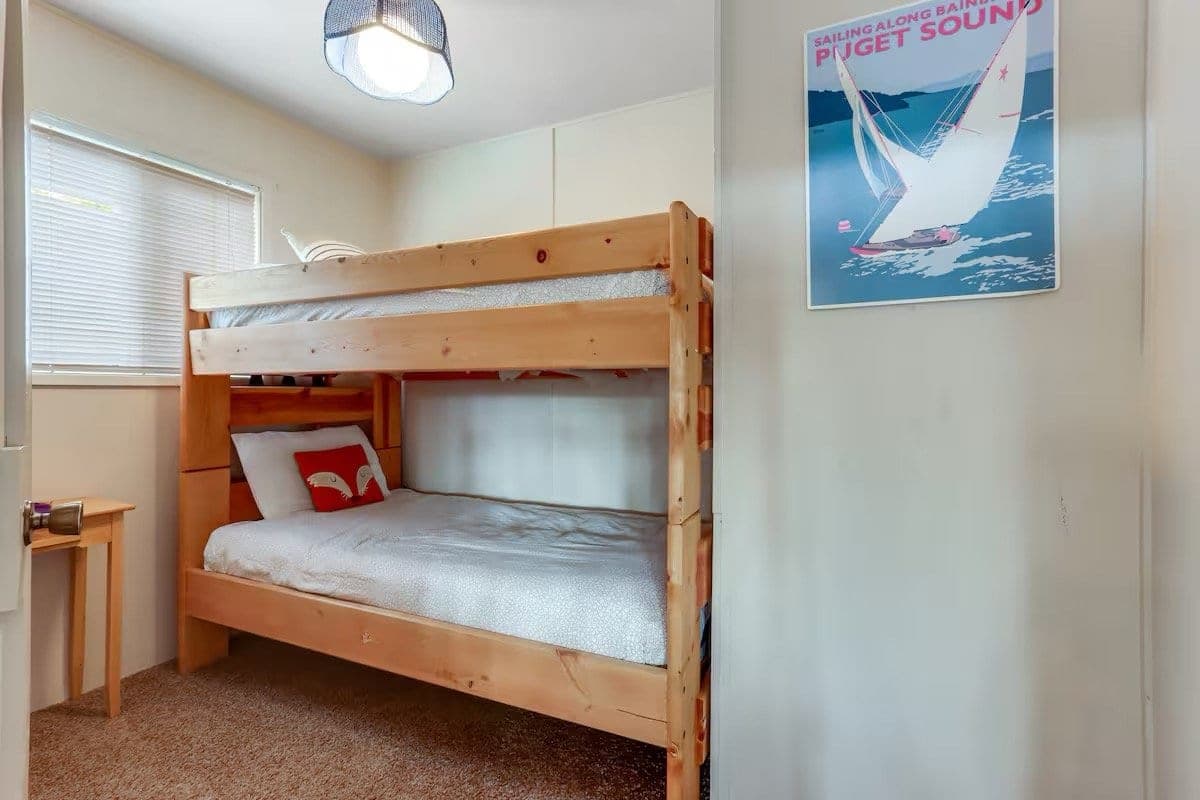 Small bedroom with a wooden bunk bed, a window with blinds and a sailing poster on the wall