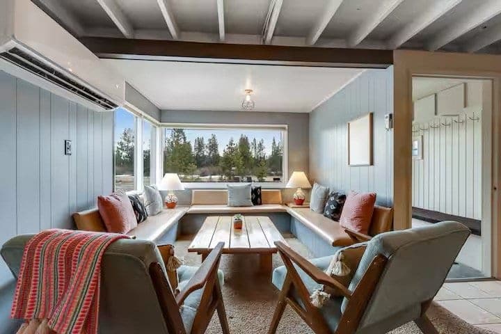 Cottage living room with a built-in window seat wrapping a corner of windows, wood coffee table and armchairs