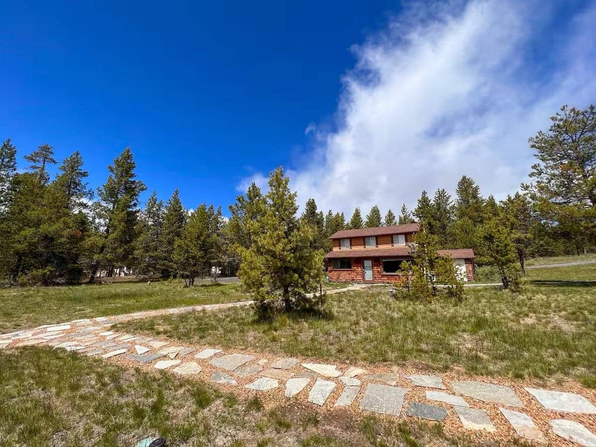The two-story cottage across a grassy clearing, a flagstone path leading toward it through the pines, Deschutes Riverfront Retreat near Sunriver, Oregon