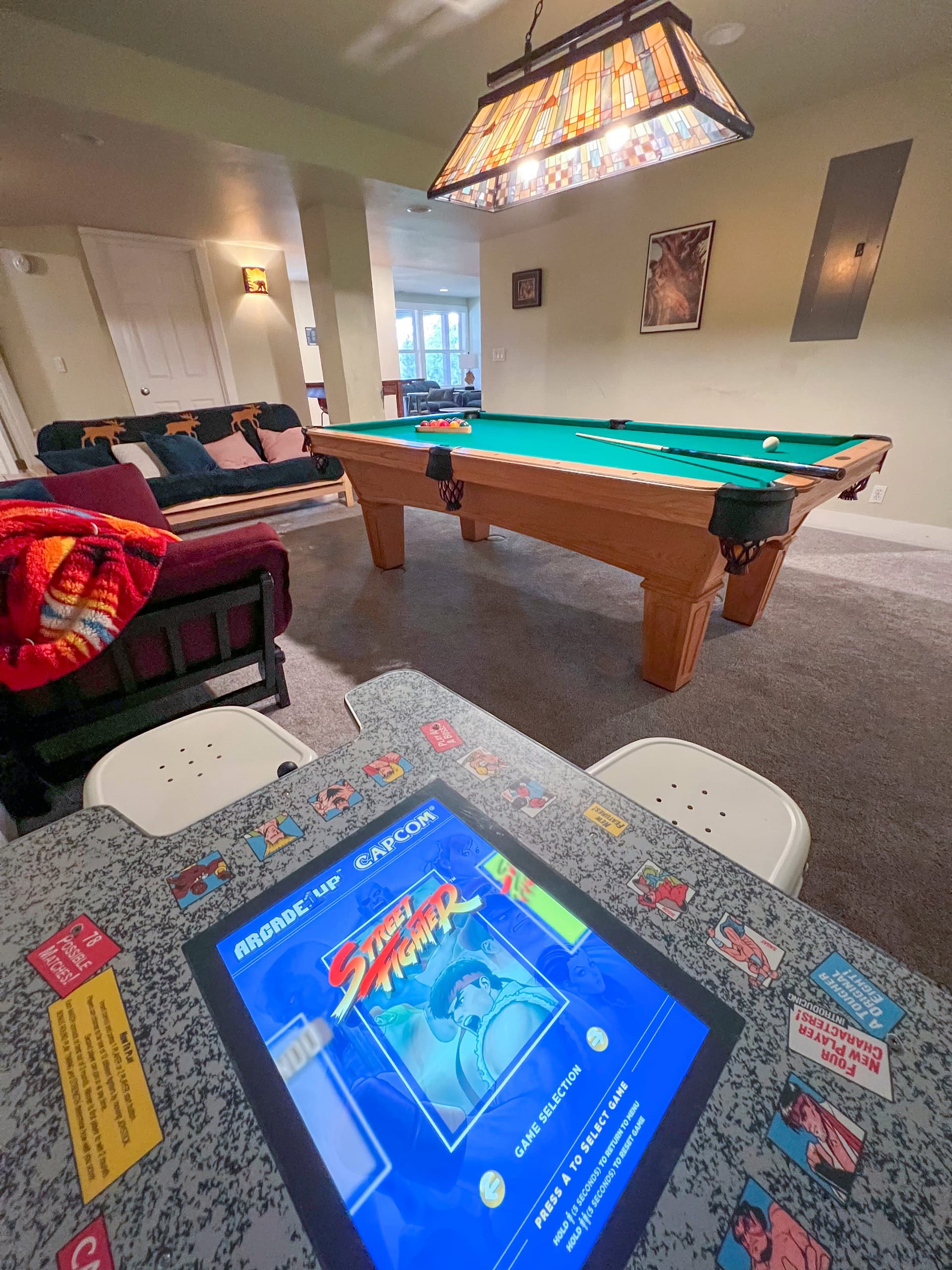 Game room with a pool table, an arcade cabinet used as a table, and lounge seating under a stained-glass lamp