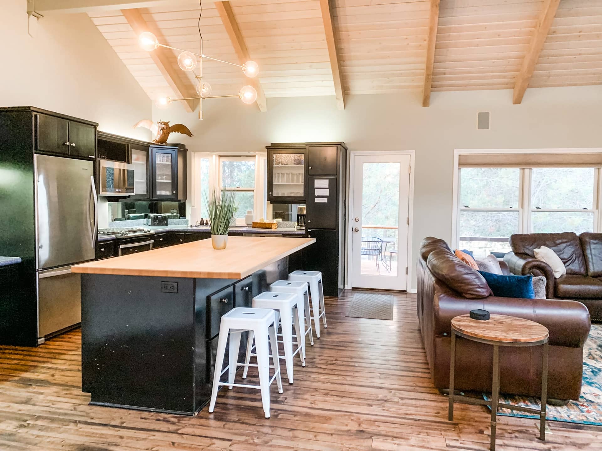 Airy vaulted kitchen with a butcher-block island, white bar stools, dark cabinets and leather seating beyond, Deschutes Riverfront Retreat near Sunriver, Oregon