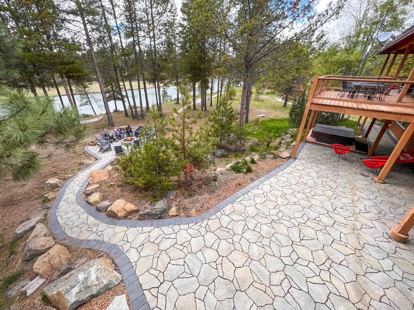 Flagstone patio curving toward the deck, with guests gathered around the fire pit down by the river, Deschutes Riverfront Retreat near Sunriver, Oregon