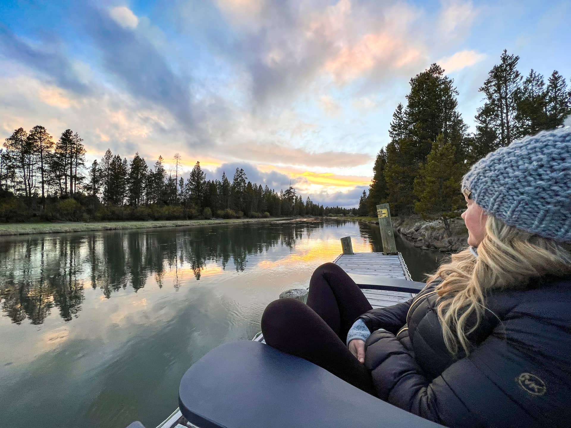 A guest in a knit hat sitting on the private dock, watching sunset colours spread across the river, Deschutes Riverfront Retreat near Sunriver, Oregon