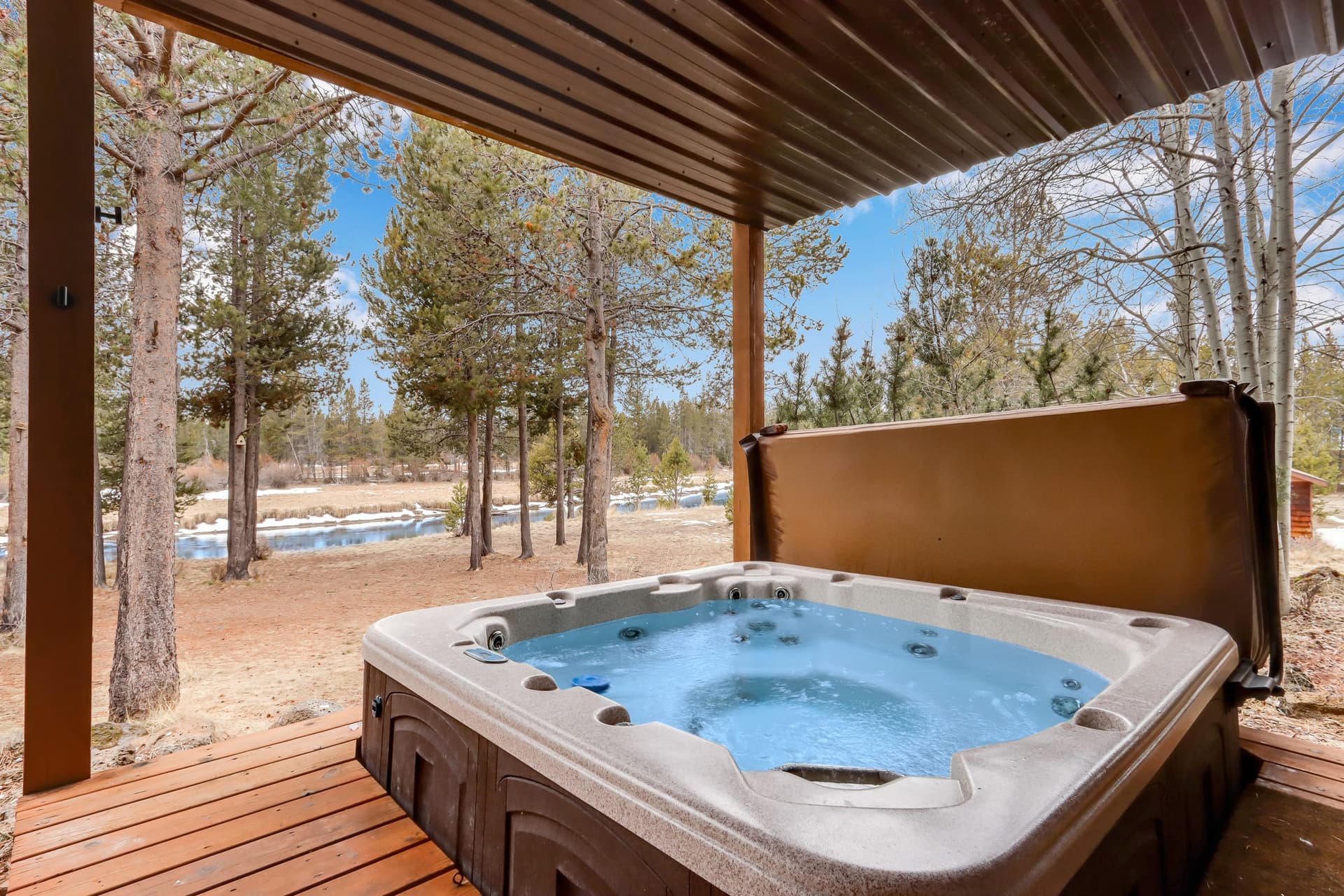 Covered hot tub on a wooden deck looking out through the pines toward the water