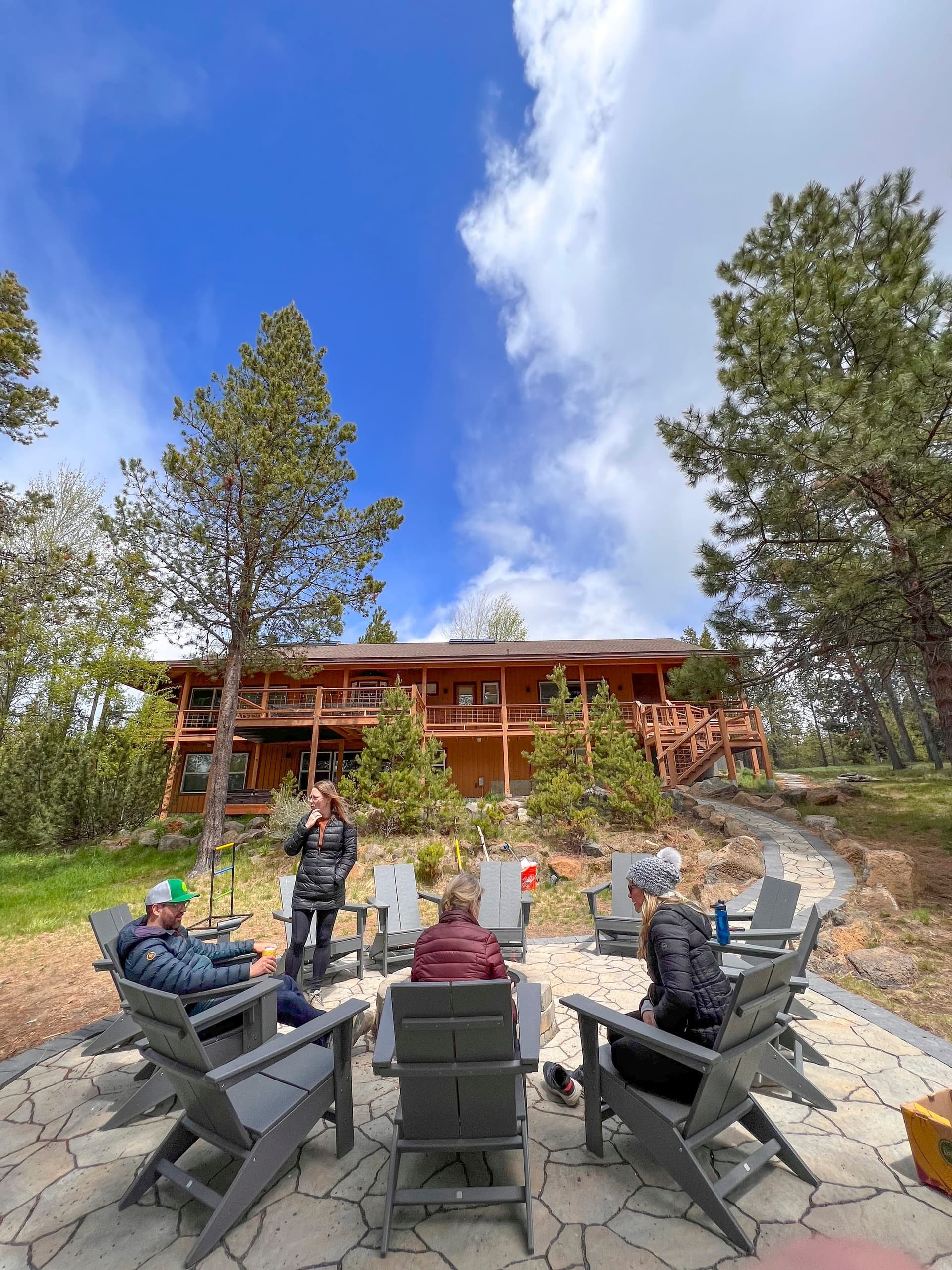 Guests seated in a circle of chairs around the fire pit on the flagstone patio, the lodge behind them