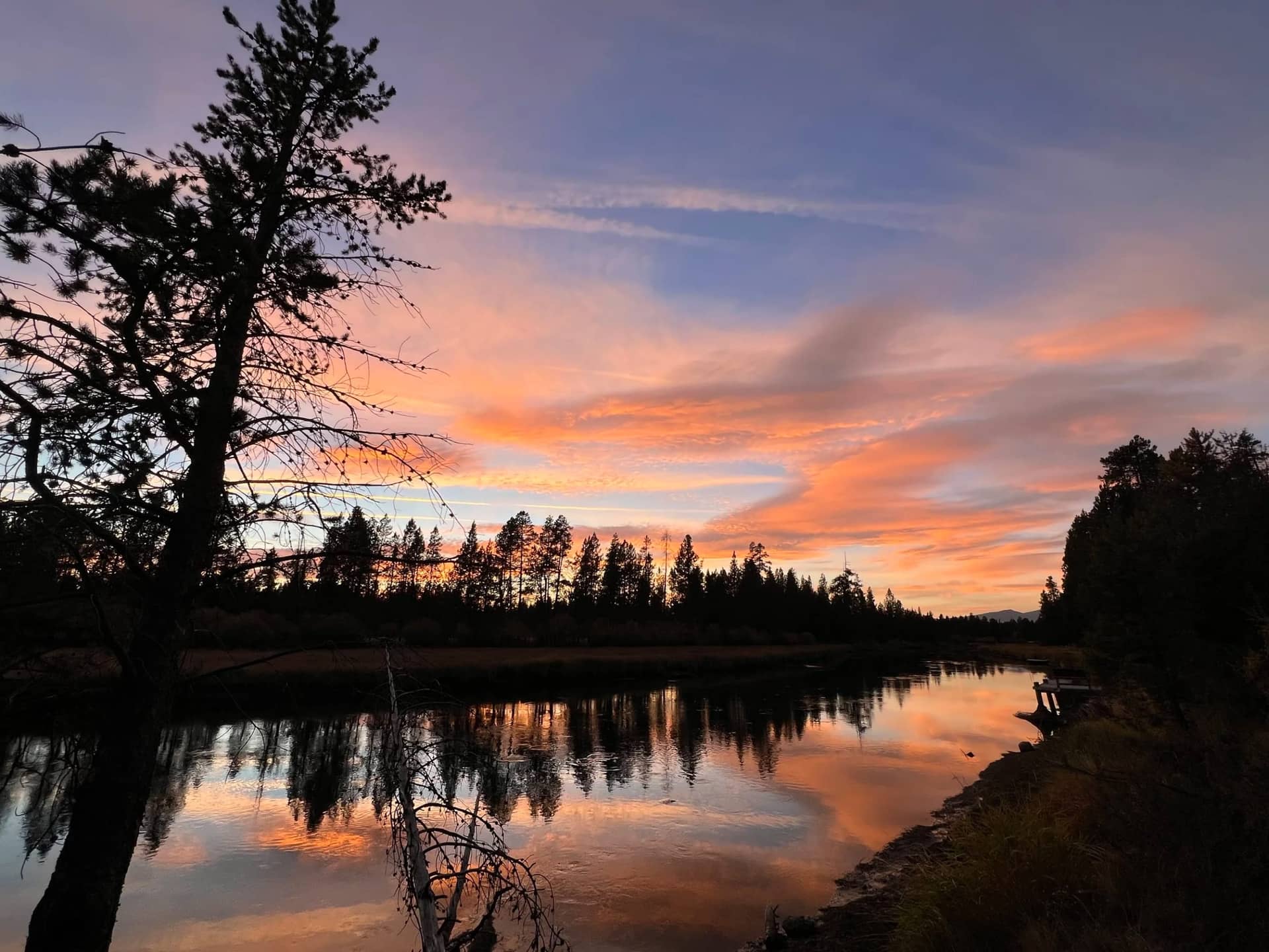 Sunset over the Deschutes River, orange cloud reflected in still water between silhouetted pines
