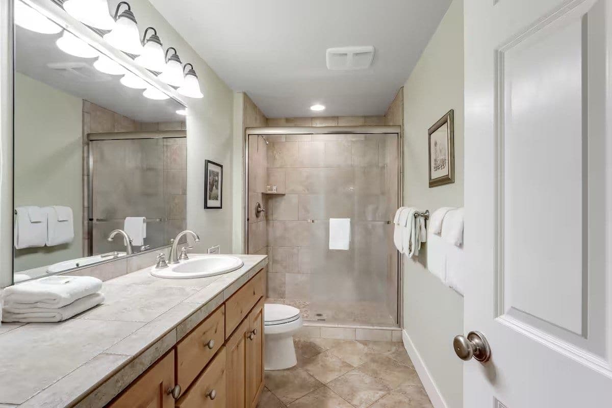 Bathroom with wooden vanity, double sink, large mirror, towel rack, and a glass-enclosed shower area.