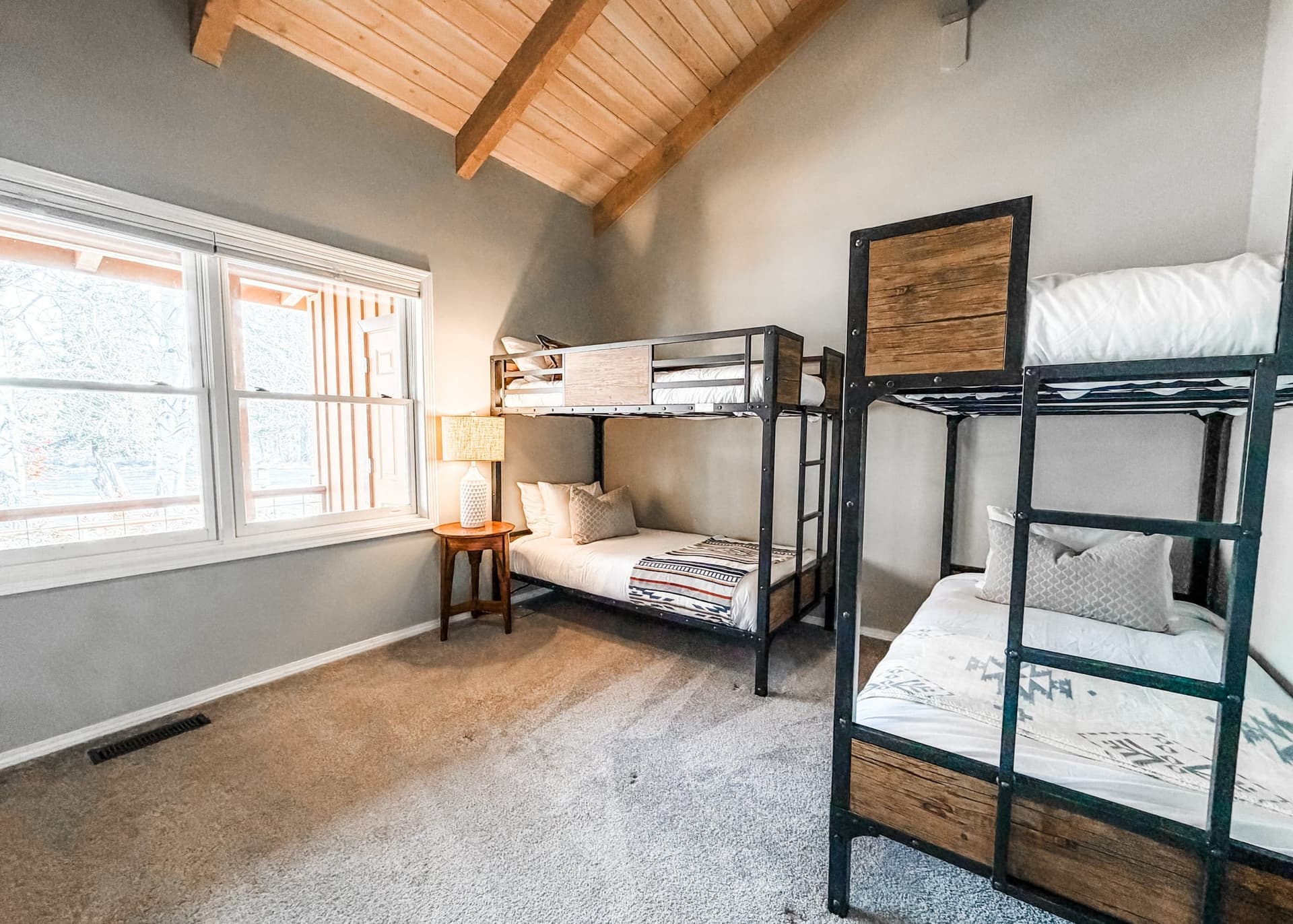 Bedroom under a vaulted wood ceiling with two metal-framed bunk beds and a window to the trees