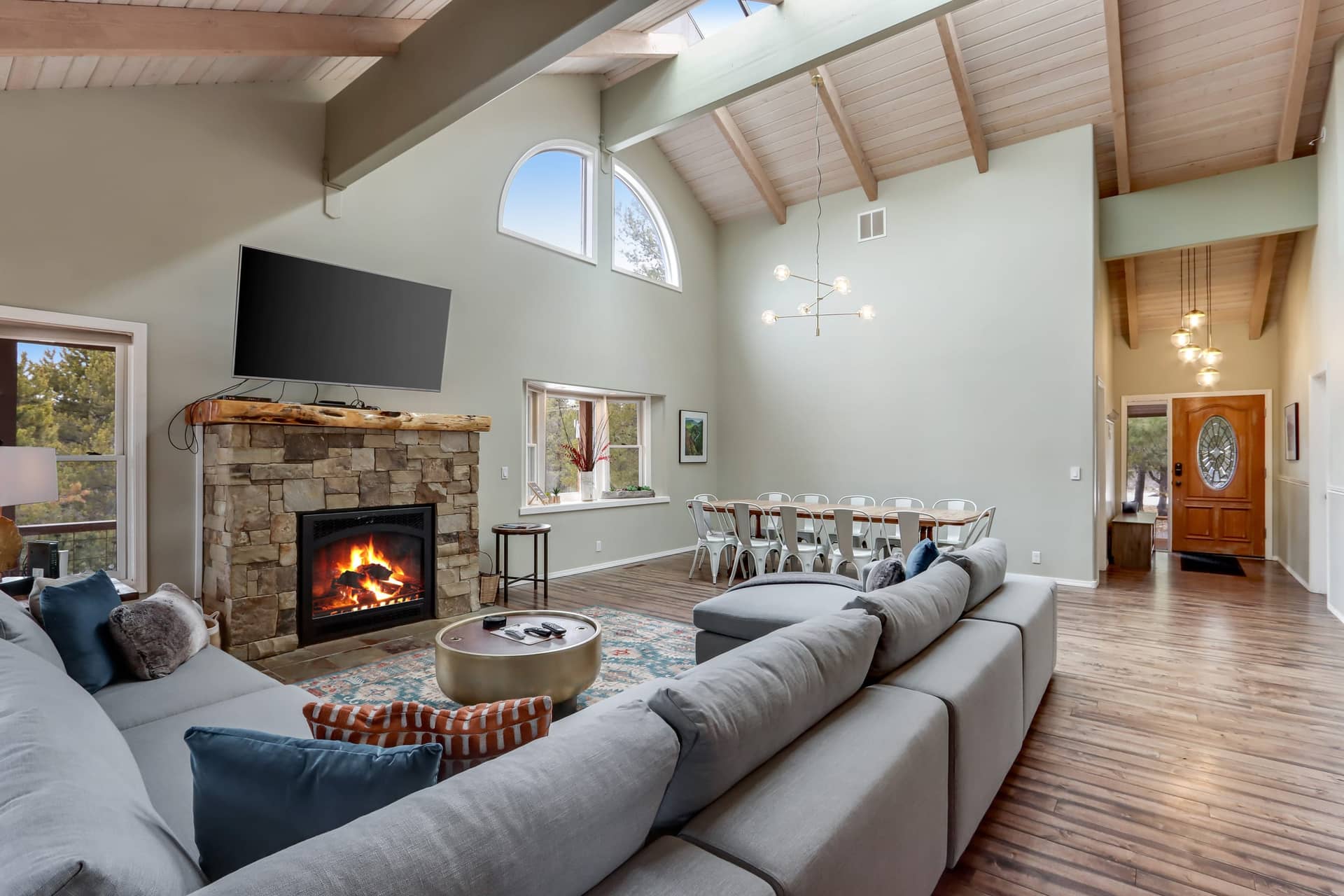Living room with a stone fireplace, a wall-mounted TV, a large sectional sofa, and a dining area with a long white table, Deschutes Riverfront Retreat near Sunriver, Oregon