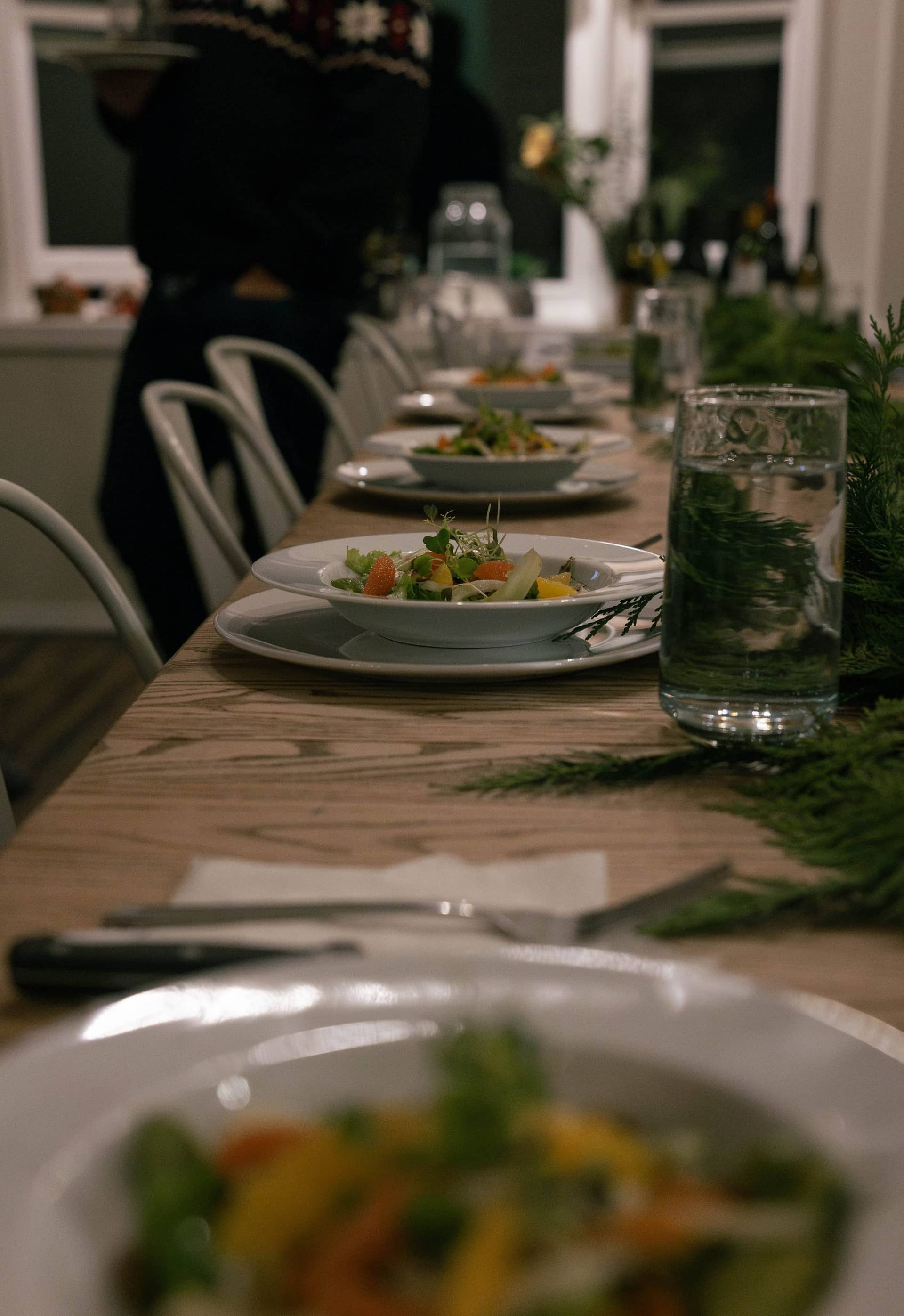 A long table set for dinner with plated salads, glassware and greenery down the centre, Deschutes Riverfront Retreat near Sunriver, Oregon